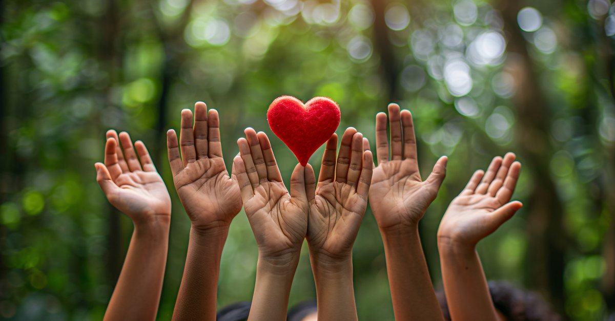 Raised hands reaching toward a red heart outdoors