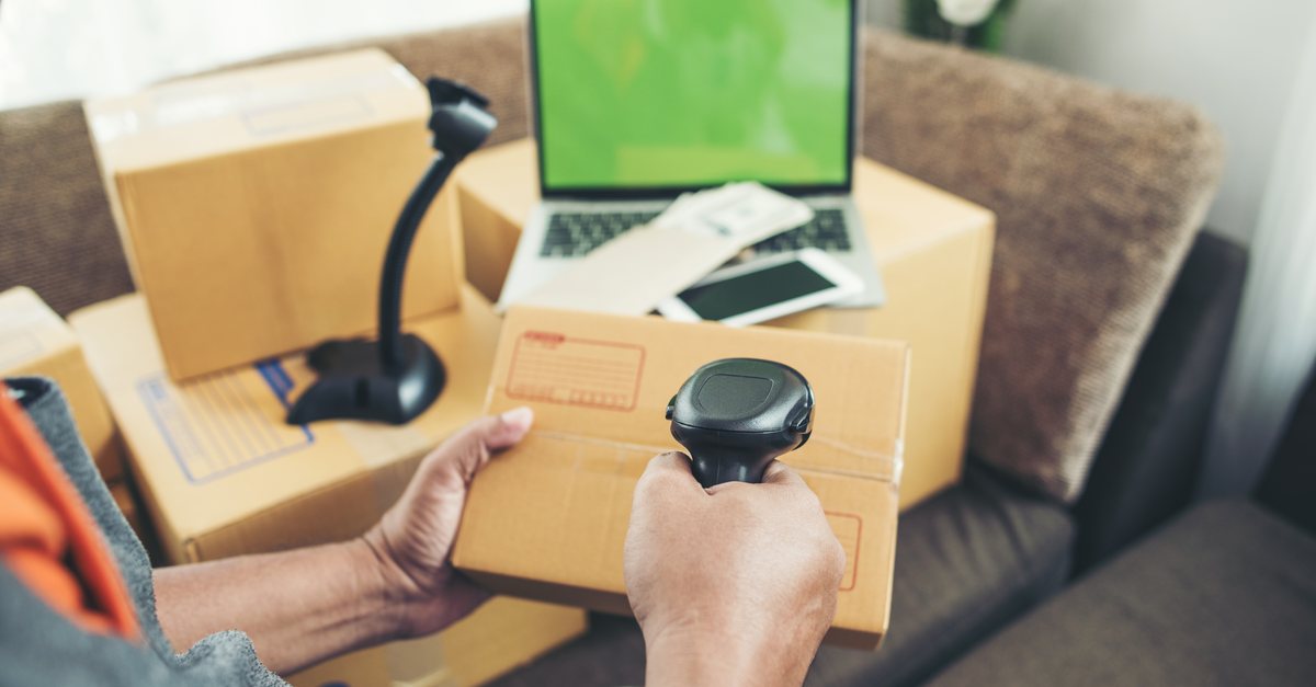 Hand scanning a parcel barcode with a laptop and boxes nearby
